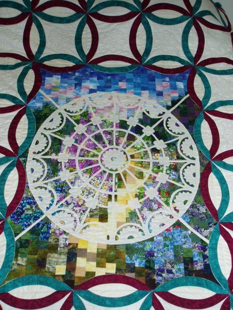 Quilt of pieces put together to show path through gate and garden flowers